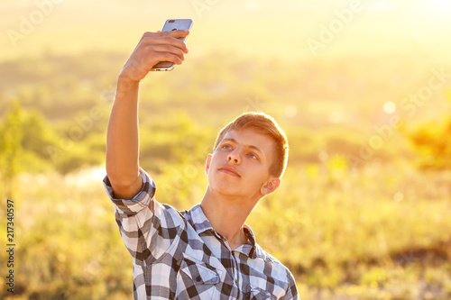 happy young man doing a selfie on the phone and smiling, natural background in the sunlight