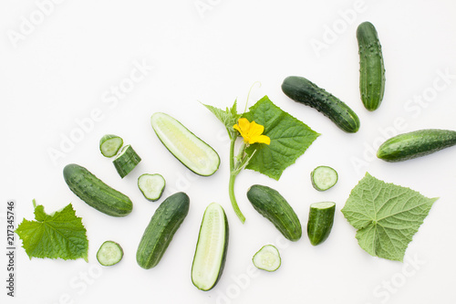 Young cucumbers with cut cucumber and leaf on white