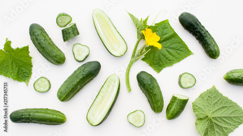 Young cucumbers with cut cucumber and leaf on white