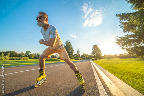 Bild auf Leinwand The elderly man in sunglasses rollerblading on the road on the sunset background