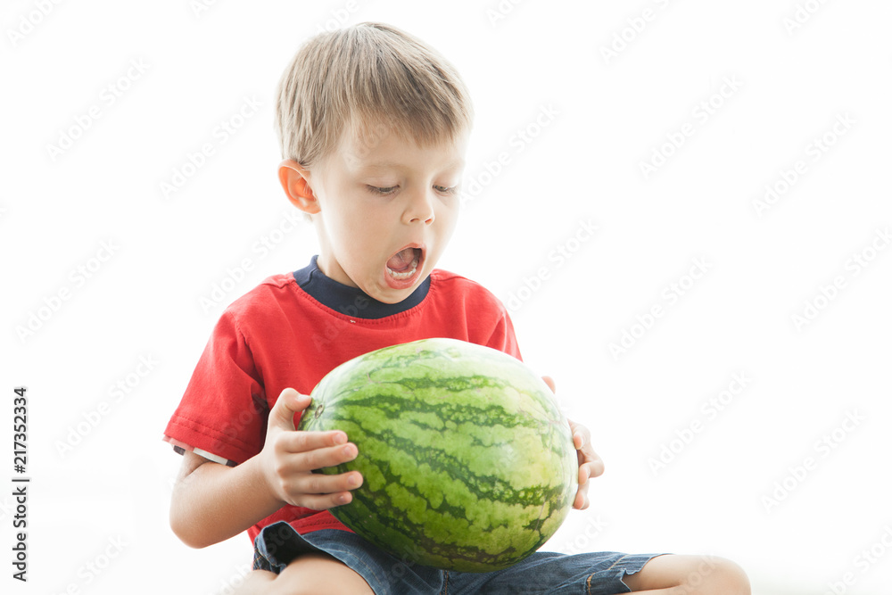 Fototapeta premium A cute boy and a big green watermelon. The child smiles and rejoices.