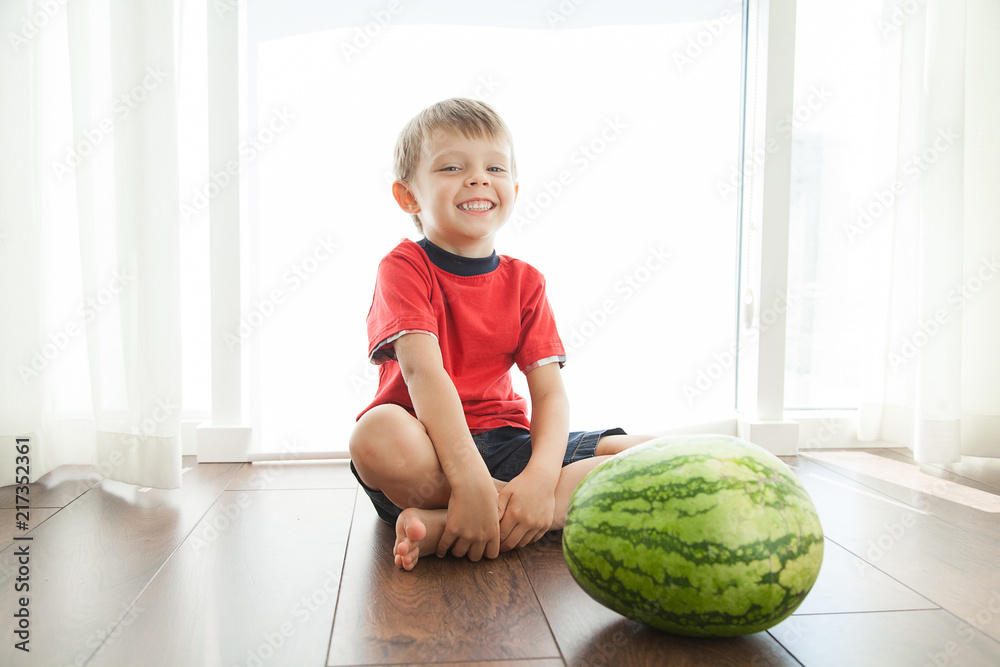 Fototapeta premium A cute boy and a big green watermelon. The child smiles and rejoices.