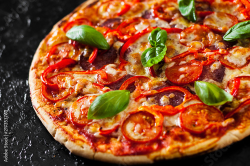 Pizza with Mozzarella cheese, Ham, Tomatoes, salami, pepper, pepperoni Spices and Fresh Basil. Italian pizza.on black background