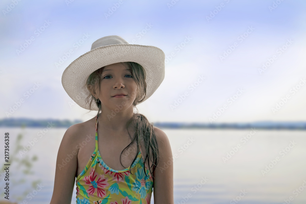 portrait of a cute little girl in a white hat with a smile on her face in summer on the beach