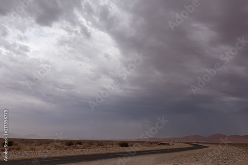 Dramatic thunderstorm rain and sandstorm over red sand dunes with asphalt road
