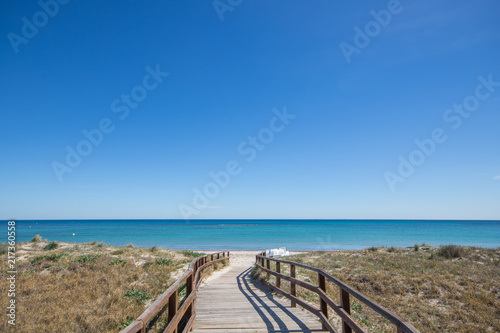 Fototapeta Naklejka Na Ścianę i Meble -  Wooden path leading to sandy beach on the Mediterranean Sea with clear blue water and sky