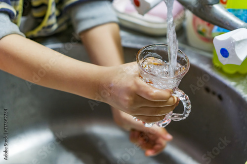 Close-up of the hands of a little boy filling a glass of water on the tap. Shallow depth of focus.