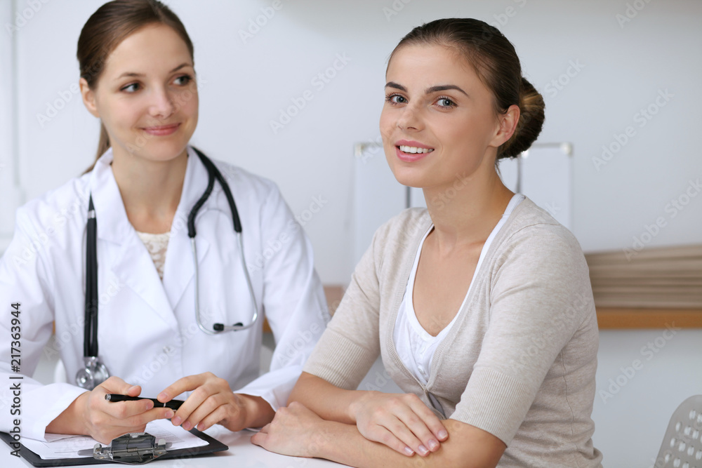 Doctor and patient having a pleasure talk while sitting at the desk at hospital office. Healthcare and medicine concept Doctor and patient having a pleasure talk while sitting at the desk at hospital office. Healthcare and medicine concept