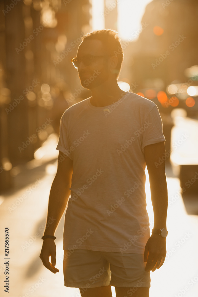 Young man with beard posing in the rays of the sunset on the old European street in Spain
