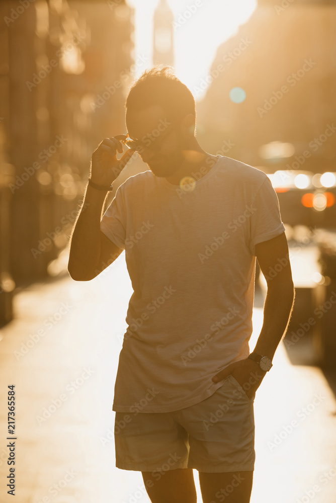 Young man with beard posing with his sunglasses in the rays of the sunset on the old European street in Spain