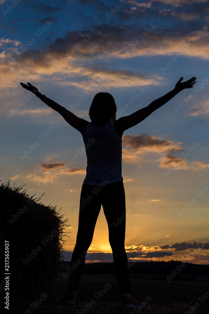 Frau spürt die Freiheit auf einem Heuballen in der Natur beim Sonnenuntergang