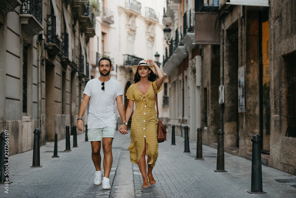 Pretty brunette girl with her boyfriend with beard walking holding hands on the old small European street in Spain on the sunset