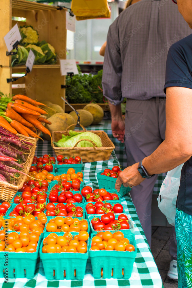 Obraz premium Variety of locally grown cherry tomatoes and carrots at Union Square Greenmarket Farmer's Market NYC with shoppers