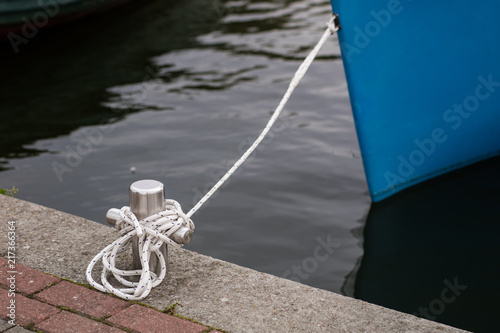 Bollard with a mooring line wrapped around it. Moored boats at the yacht harbor.