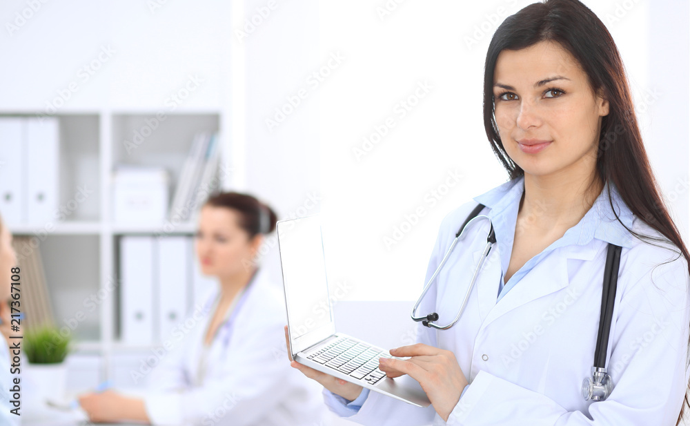 Brunette female doctor on the background of colleagues talking to each other in hospital. Medicine and health care concept Brunette female doctor on the background of colleagues talking to each other in hospital. Medicine and health care concept