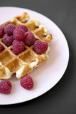 Traditional belgian waffle with raspberries on pink plate over black surface, closeup.