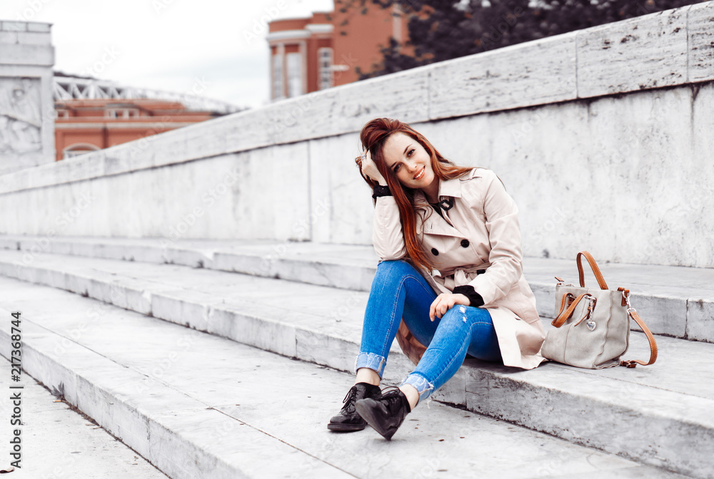 Beautiful model sitting on the ground in the centre of Rome,Italy. Young lady with adorable smile posing in front of a camera. Red hair girl strolling around the ancient Roman city. Italian fashion