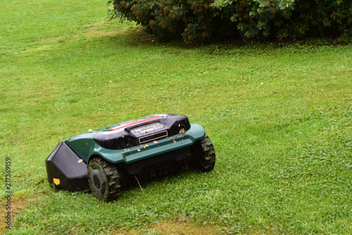 Robot lawnmower in the garden on the slope in the rain.