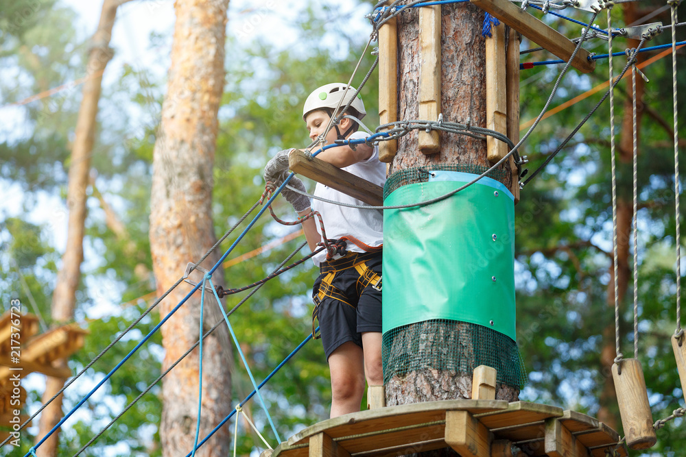 cute boy in white t shirt in the adventure activity park with helmet and safety equipment. Young boy playing and having fun doing activities outdoors. Hobby, active lifestyle concept cute boy in white t shirt in the adventure activity park with helmet and safety equipment. Young boy playing and having fun doing activities outdoors. Hobby, active lifestyle concept