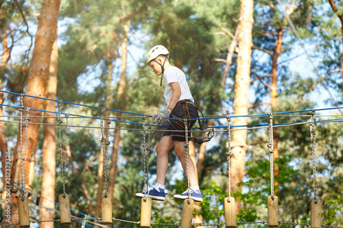 cute boy in white t shirt in the adventure activity park with helmet and safety equipment. Young boy playing and having fun doing activities outdoors. Hobby, active lifestyle concept