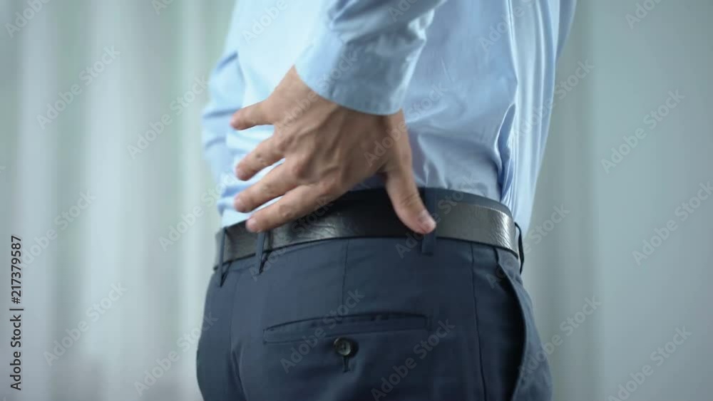 Male office worker feeling sharp back pain, standing up, sedentary lifestyle Male office worker feeling sharp back pain, standing up, sedentary lifestyle