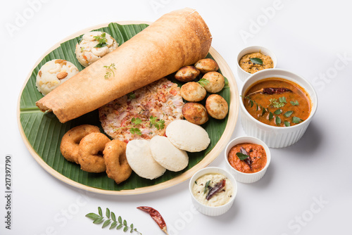 Group of South Indian food like Masala Dosa, Uttapam, Idli/idly, Wada/vada, sambar, appam, semolina halwa, upma served over banana leaf with colourful chutneys, selective focus