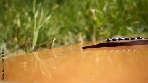 Acoustic guitar with wooden finish in slow motion in nature and grassy riverside.
