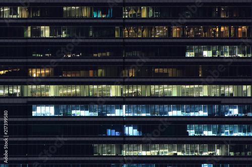 workers in a box. office building light at night. multistory modern glass and metal clad office building light up at night.