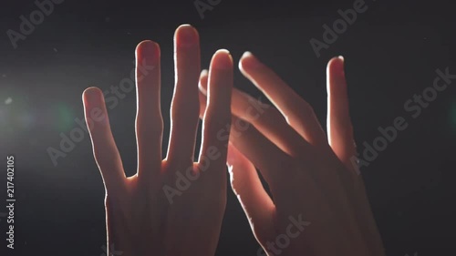 Silhouette portrait of two caucasian female hands closeup raised upward and playing in light with flying dust into air, isolated over black background