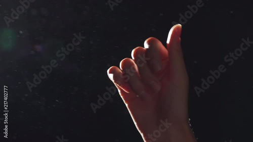 Portrait of european female hand closeup raised upward and playing in light with flying dust into air, isolated over black background