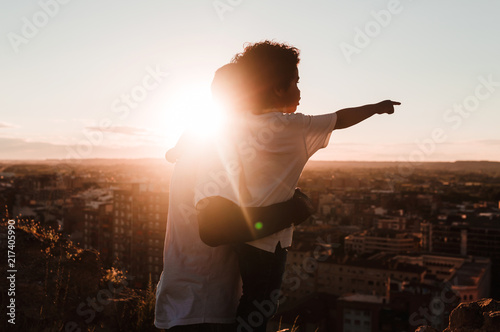 Father and son in a cliff observing the city in a sunset of summer, builds background photo