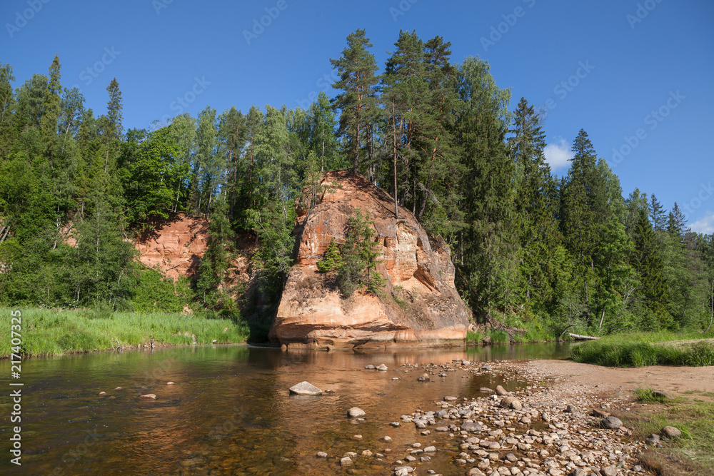 Summer landscape and red stone cliff of Zvartes in the basin of Amata river, Latvia, Europe. Daytime.