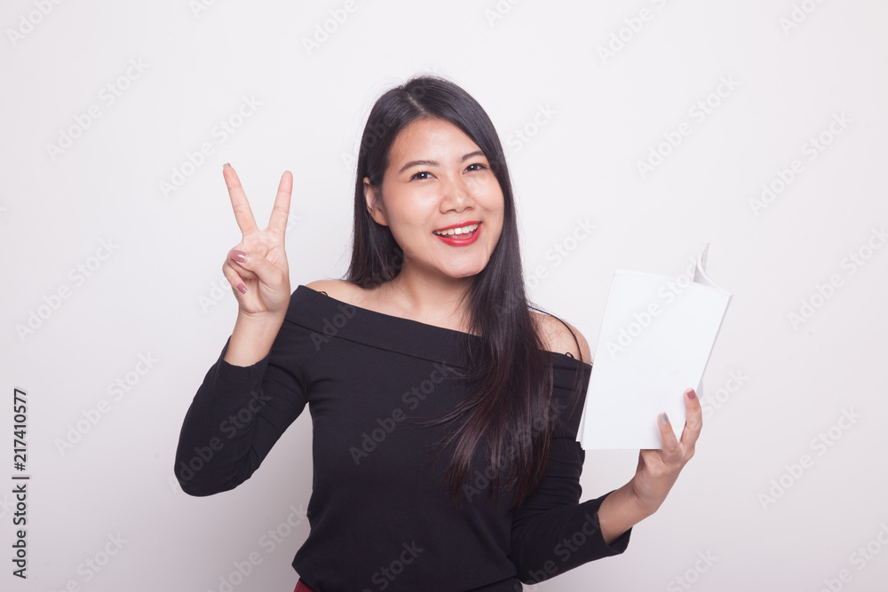 Young Asian woman show victor sign with a book. Young Asian woman show victor sign with a book.