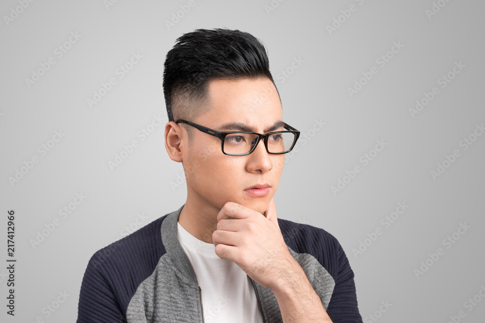 A portrait of a young asian man thinking looking down isolated over gray background A portrait of a young asian man thinking looking down isolated over gray background
