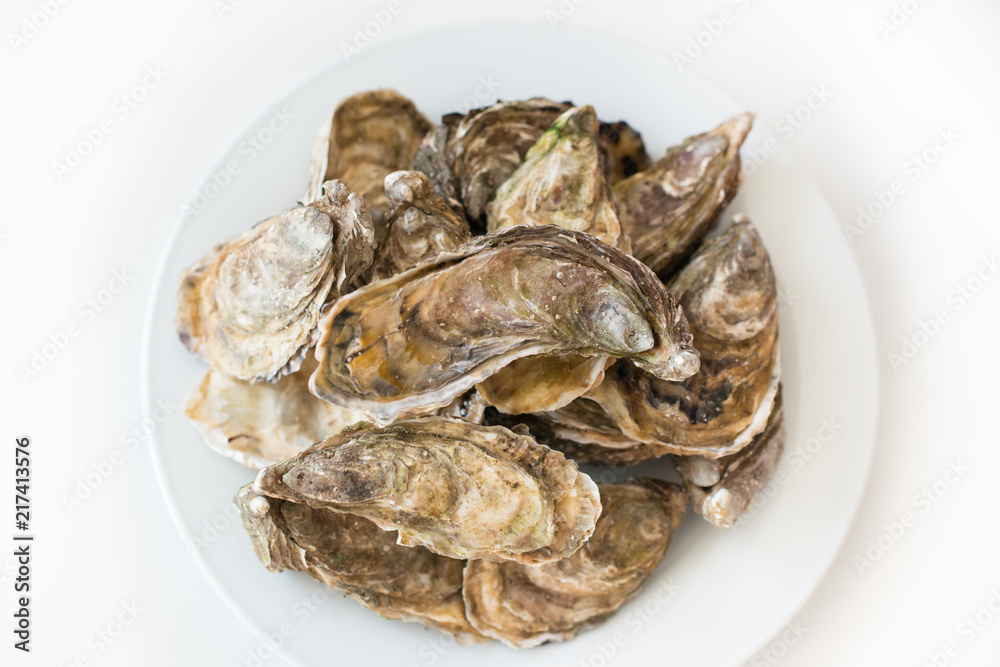 Fresh oysters. Raw fresh oysters on white round plate, image isolated, with soft focus. Restaurant delicacy. Saltwater oysters. Fresh oysters. Raw fresh oysters on white round plate, image isolated, with soft focus. Restaurant delicacy. Saltwater oysters.