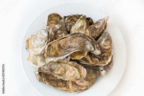 Fresh oysters. Raw fresh oysters on white round plate, image isolated, with soft focus. Restaurant delicacy. Saltwater oysters.