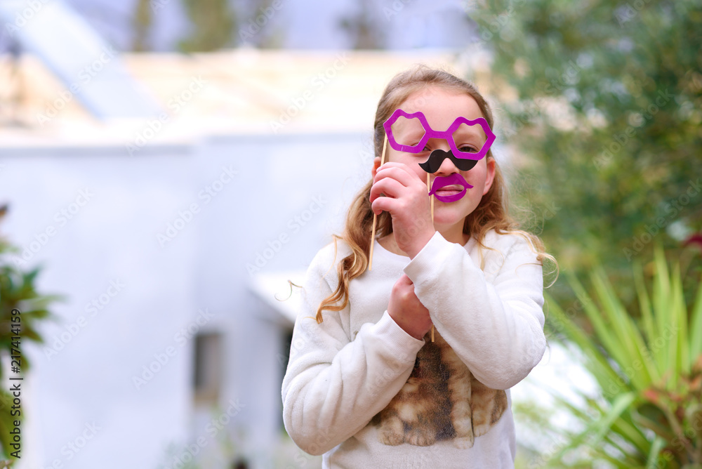 Funny little girl with fake moustache,lips and glasses paper mask. Kids birthday, Halloween Father day, Purim, Fool day concept. Suitable for greeting card, invitation, poster, proposing. Funny little girl with fake moustache,lips and glasses paper mask. Kids birthday, Halloween Father day, Purim, Fool day concept. Suitable for greeting card, invitation, poster, proposing.