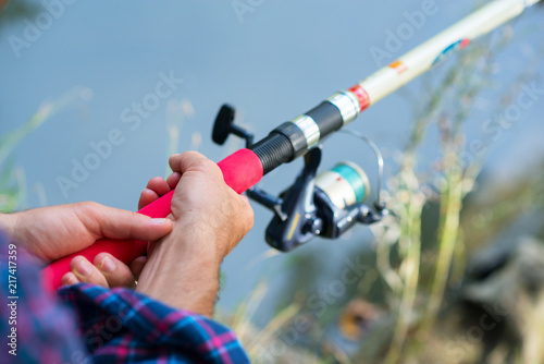 Man fishing at river bank, summer outdoor. Summer leisure, hobby. Fishing. Angling. Man's hand with fishing rod over light green lake water with copyspace.