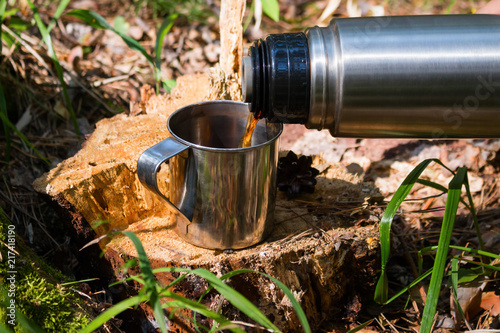 traveler in the forest pours tea from thermos