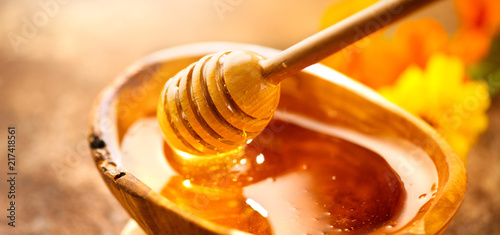 Honey. Healthy organic thick honey dripping from the honey dipper in wooden bowl. Sweet dessert background
