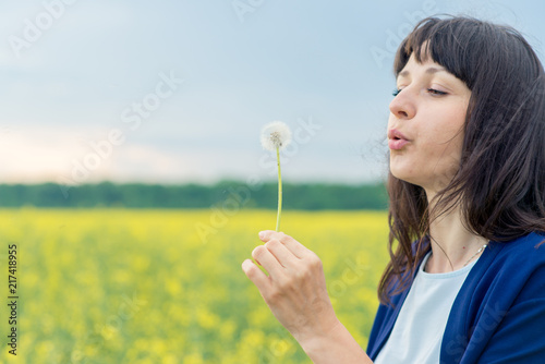 young emotional beautiful sensual pretty girl in a white shoe and in a blue cape top, with dark hair on the yellow yellow reed field with a dandelion in his hands