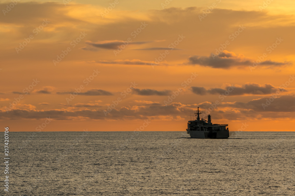 Large supply and support navy ship sail along the sea in the evening before sunset. Silhouette view.