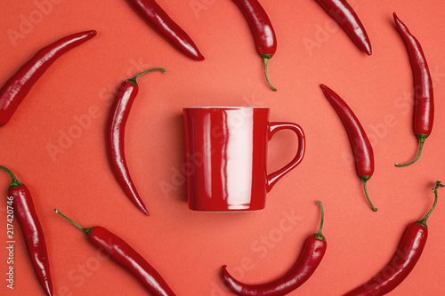 Red coffee mug surrounded by chili peppers on a red background.