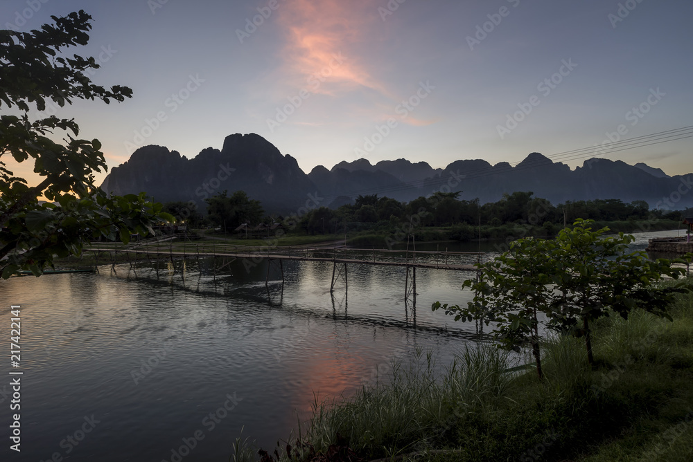 Beautiful sunset with colorful cloud reflected in the Nam Song river and wooden bridge, Vang Vieng, Laos Beautiful sunset with colorful cloud reflected in the Nam Song river and wooden bridge, Vang Vieng, Laos
