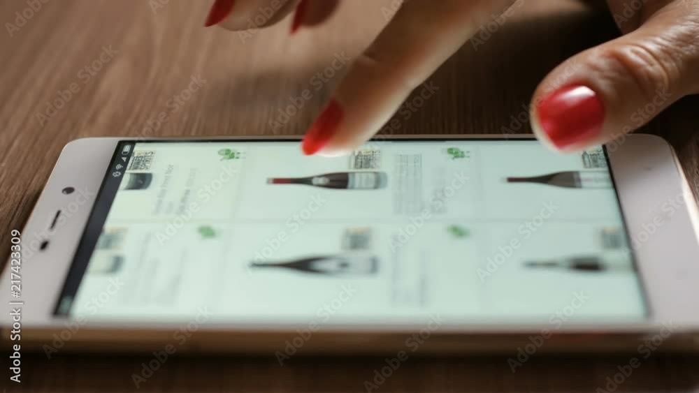 Woman orders red wine home in an online store. Female selects the alcohol in the grocery online store. Close-up. 4K UHD. Screen is blurred.