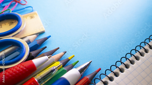 School supplies on blue background. Pens, pencils, scissors, ruler, paper clips, notebook and marker on the table. View from above with copy space