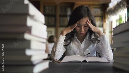 Tired female asian sudent lawyer in white shirt trying to concentrate reading books in the library. Portrait. Indoors.