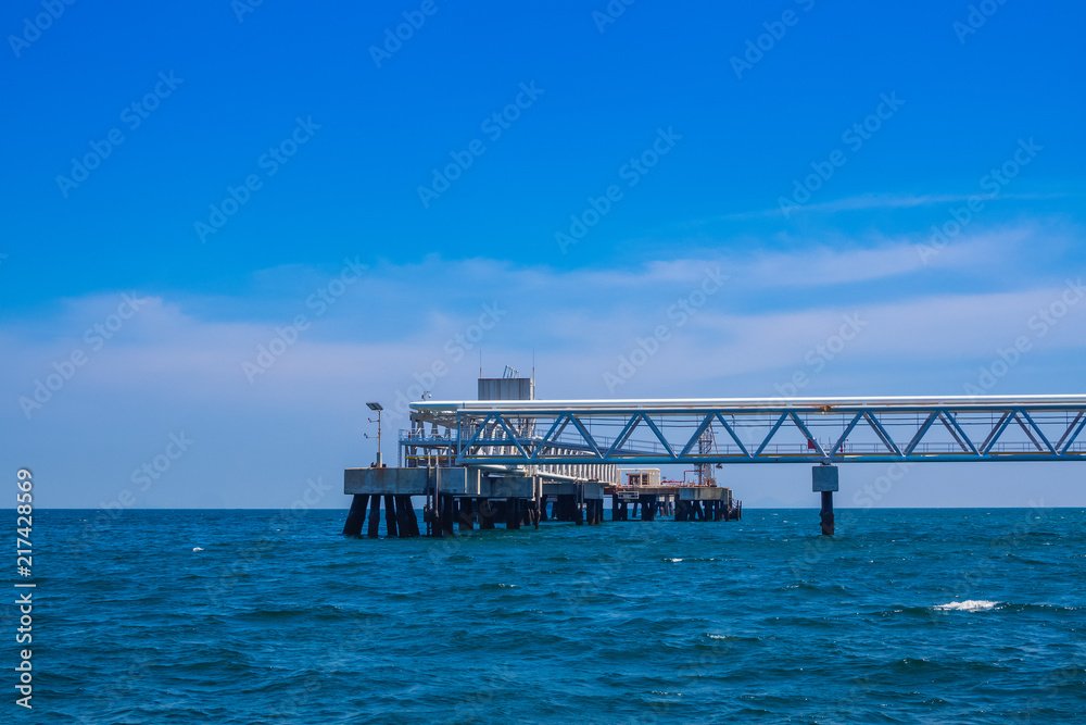 Oil fuel pipeline tube on jetty to the sea and blue sky background