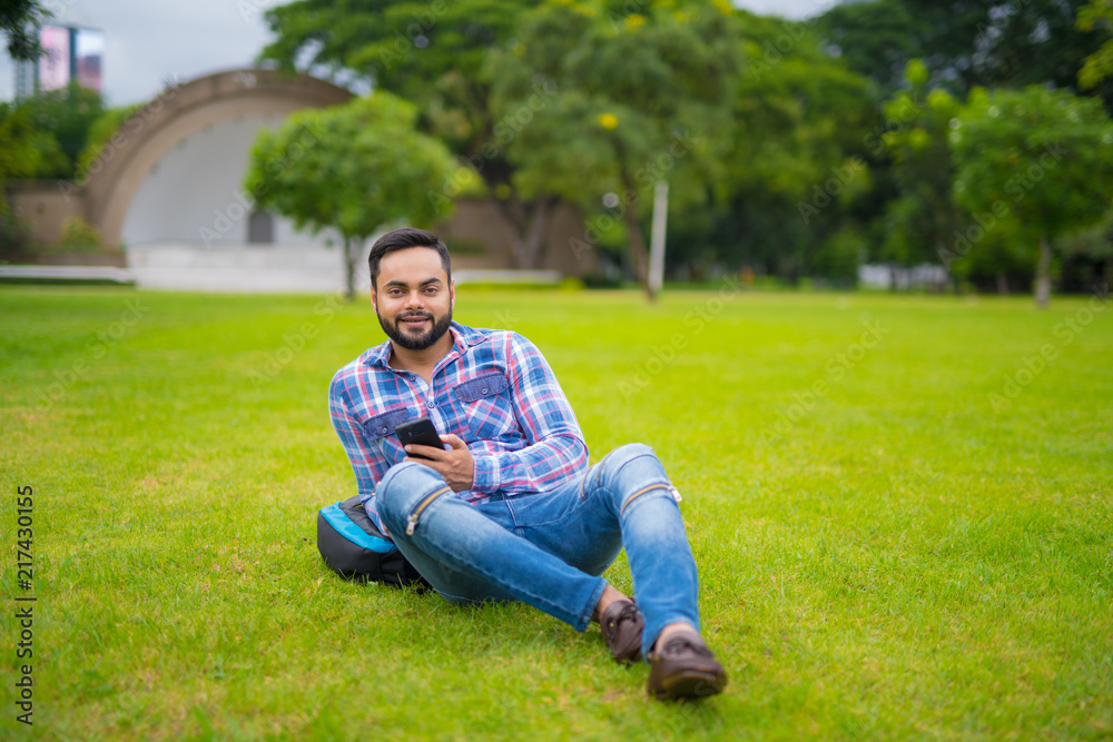 Handsome Indian Man In Park Lying Down On Grass And Holding Mobile Phone Handsome Indian Man In Park Lying Down On Grass And Holding Mobile Phone