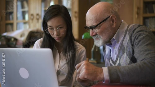 biologist Professor and female student are talking at table with laptop in library, elderly man and young woman are discussing scientific topic, sitting at desk with PC in reading room. Concept